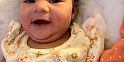 Angel is registered to the contest to win money with this photo: baby, smiling, child, floral_clothing, infant, face, skin, lying_down, cute, portrait, happy, soft_fabric, patterned_clothing, person, indoors, young_child, closeup, head, cheeks, warm_colors