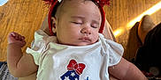 Angel is registered to the contest to win money with this photo: baby, blue, celebration, closeup, clothing, cute, festive, headband, heart, indoors, infant, lap, person, pom_poms, red, resting, sleeping, stars, white, wooden_floor