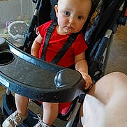 River is registered to the contest to win money with this photo: toddler, stroller, child, red_shirt, sneakers, blue_eyes, baby_shoes, seat_belt, indoor, person, footwear, furniture, curious, candid, plastic_tray, leg, baby, expression, sitting, young_child