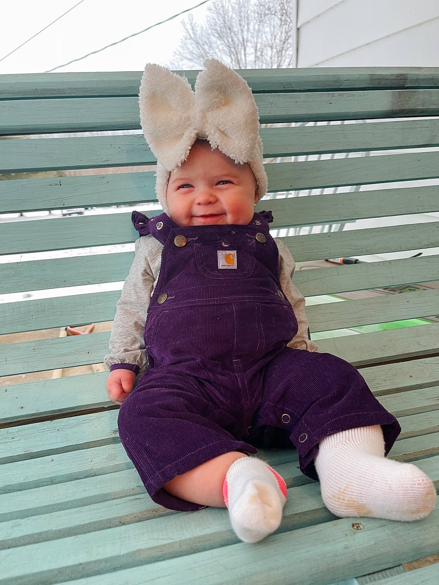 Kora is registered to the contest to win money with this photo: baby, baby_toddler_clothing, cap, cheek, child, face, foot, fun, fur, grass, happy, hat, headwear, person, pink, purple, sitting, sleeve, smile, toddler