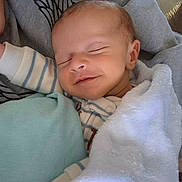 Merritt is registered to the contest to win money with this photo: baby, sleeping, smiling, blanket, pillow, cozy, infant, child, cute, soft, resting, peaceful, wearing_clothes, striped_clothing, face, head, skin, hand, comfort, indoors