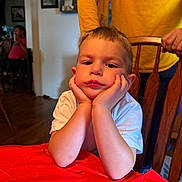Dean joined the competition — help win amazing prizes! child, boy, bored, white_shirt, table, red_tablecloth, chair, wooden_chair, hands_on_face, indoor, person, adult_hand, yellow_shirt, home, living_room, portrait, expression, furniture, face, casual