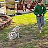 child, dog, leash, cone, grass, backyard, barefoot, hoodie, playful, smiling, pet, outdoor, furniture, grill, adventure, sunlight, casual, happy, young, nature