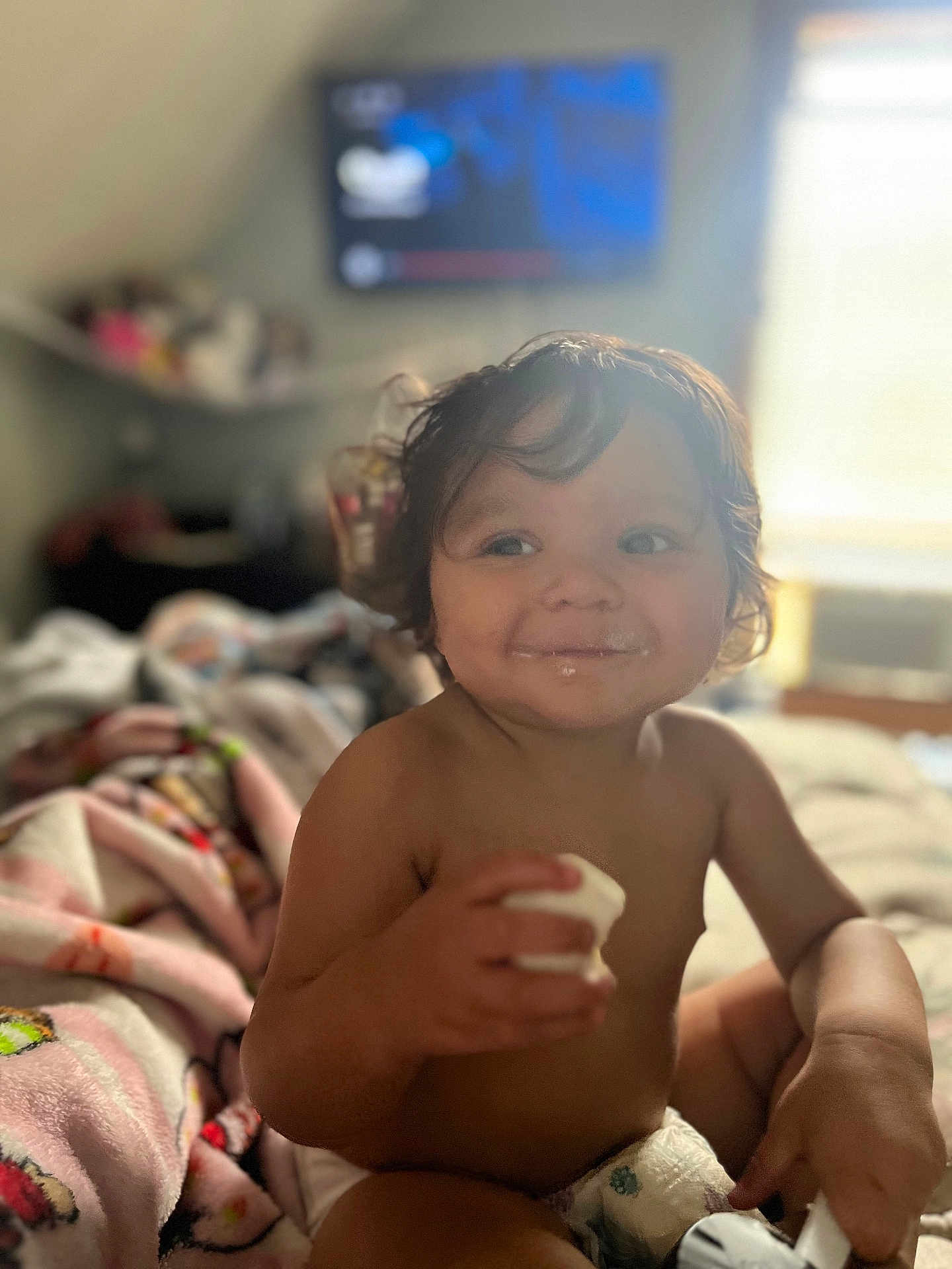 Mateo joined the competition — help win amazing prizes! toddler, child, smile, indoors, bed, blanket, diaper, food, milk_mustache, hand, hair, face, expression, cheeky, happy, cozy, soft_light, blurred_background, furniture, room