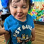 Mateo is registered to the contest to win money with this photo: child, toddler, blue_shirt, flower_headband, smiling, indoor, wooden_floor, colorful_background, best_buddies, cartoon_characters, short_hair, green_skirt, hand, face, cute, person, portrait, clothing, happy, standing