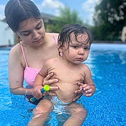 Mateo joined the competition — help win amazing prizes! child, toddler, woman, pool, water, swimsuit, outdoor, summer, toy, wet_hair, baby, holding, blue_sky, clouds, nature, skin, expression, person, family, recreation