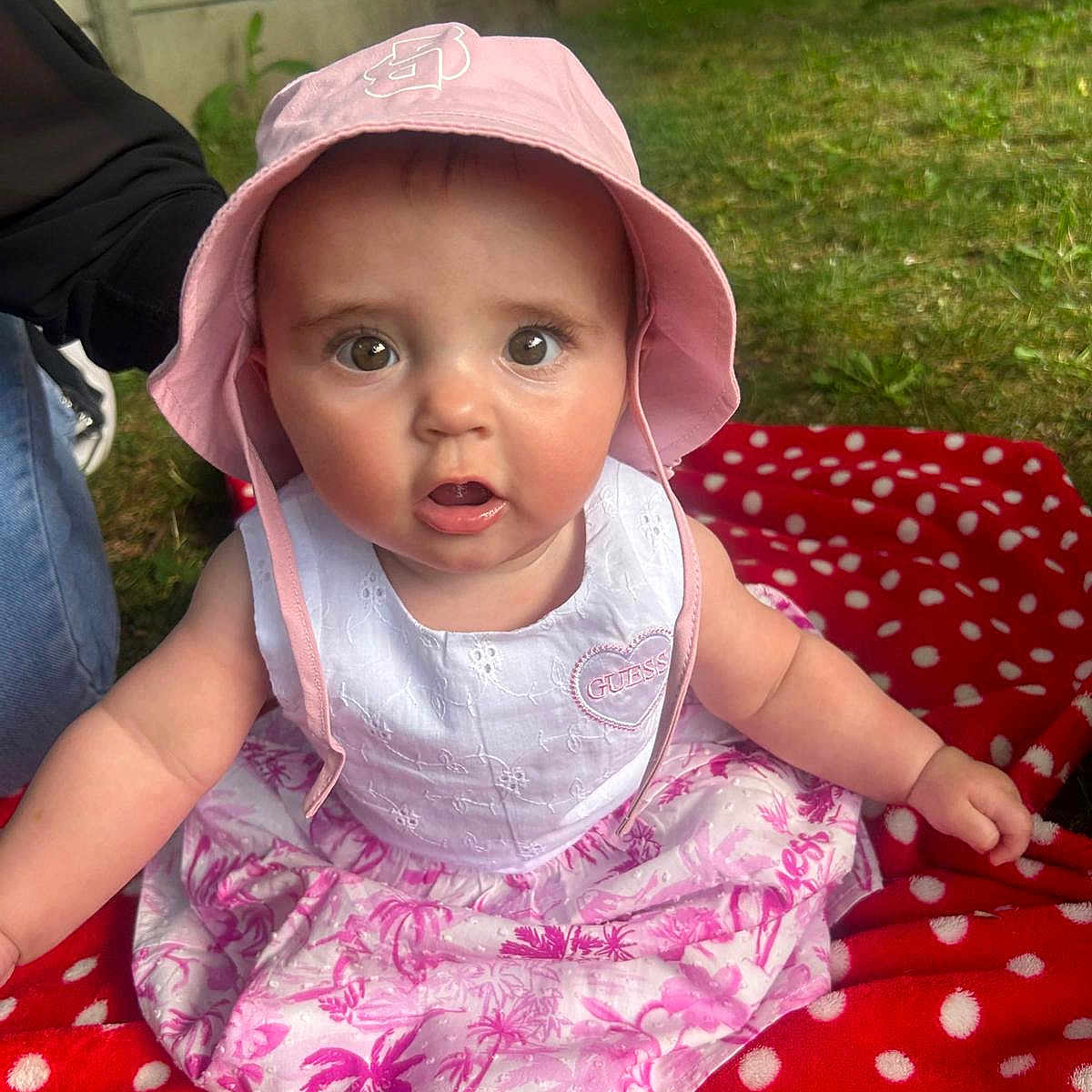 Giulia a rejoint le concours — aidez-le/la à gagner de superbes lots ! apparel, baby, blanket, child, curious, cute, dress, expression, face, grass, headwear, nature, outdoor, person, pink_hat, polka_dot, sitting, skin, summer, young_child