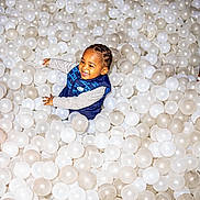 Khari joined the competition — help win amazing prizes! toddler, child, smiling, happy, ball_pit, plastic_balls, play, indoor, fun, joy, person, braided_hair, vest, long_sleeve_shirt, white_balls, dirty_balls, play_area, recreation, cute, excited