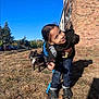 Kameron is registered to the contest to win money with this photo: child, smiling, outdoor, dog, leash, grass, blue_sky, building, brick_wall, hoodie, jeans, crocs, playful, person, pet, nature, sunny, shadow, trees, car