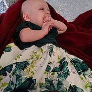 Rhyleigh is registered to the contest to win money with this photo: baby, blanket, butterflies, child, couch, cozy, dress, fingers, floral_pattern, hands, happy, home, indoor, infant, lying_down, pillow, portrait, red_blanket, sitting, smiling