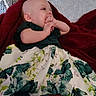 baby, blanket, butterflies, child, couch, cozy, dress, fingers, floral_pattern, hands, happy, home, indoor, infant, lying_down, pillow, portrait, red_blanket, sitting, smiling