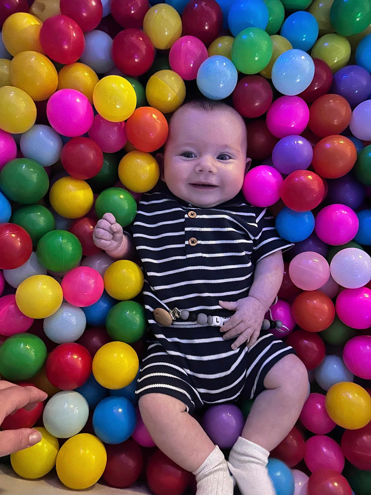 Lukasz is registered to the contest to win money with this photo: baby, child, smiling, ball_pit, colorful, plastic_balls, striped_clothing, socks, hand, play, indoor, cute, infant, happy, person, portrait, toy, fun, bright, leisure
