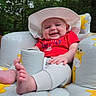 baby, infant, hat, red_shirt, inflatable_chair, giraffe_print, outdoor, greenery, trees, happy, smiling, cute, child, legs, feet, summer, nature, relaxing, sun_hat, joy