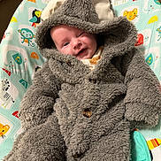 Henry is registered to the contest to win money with this photo: baby, infant, child, costume, plush, hood, smile, winking, animal_print, baby_seat, colorful, happy, cute, soft, clothing, button, face, portrait, indoors, cozy
