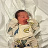 Malakai is registered to the contest to win money with this photo: newborn, baby, sleeping, infant, onesie, dinosaur_print, blanket, cozy, indoor, cute, child, soft, resting, clothing, floor, wooden_floor, peaceful, small, person, portrait