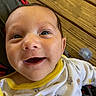 baby, infant, smile, face, closeup, eyes, clothing, yellow_trim, animal_prints, pacifier, wooden_background, happy, cute, child, person, portrait, young, skin, mouth_open, indoors
