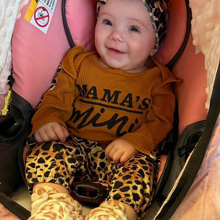 Natalie joined the competition — help win amazing prizes! baby, infant, smiling, leopard_print, headband, brown_shirt, stroller, pink_cushion, cozy, cute, child, footwear, socks, happy, portrait, indoors, person, seated, clothing, baby_clothes