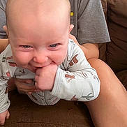 Trinity is registered to the contest to win money with this photo: baby, child, infant, hand, couch, person, clothing, onesie, animal_print, face, smile, chewing, adult, holding, arm, sitting, indoor, casual, fabric, skin