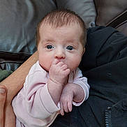 Amelia is registered to the contest to win money with this photo: baby, infant, hand, face, eyes, pink_clothing, couch, arm, person, skin, fingers, closeup, newborn, cute, indoor, portrait, human, holding, soft, cozy