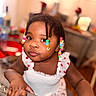 baby, child, infant, portrait, sitting, indoors, braids, beaded_hair, colorful_beads, dress, white_clothing, smiling, facial_expression, dark_skin, brown_eyes, furniture, chair, home, close_up, photography