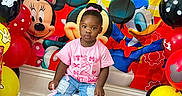 Leyana is registered to the contest to win money with this photo: child, toddler, birthday, birthday_party, balloons, cartoon, minnie_mouse, mickey_mouse, donald_duck, party_decoration, pink_shirt, jeans, pink_shoes, sitting, portrait, smiling, indoors, colorful, wooden_floor, gift_wrap
