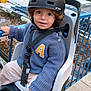 Ziggy a rejoint le concours — aidez-le/la à gagner de superbes lots ! bike_seat, blue_sweater, casual_wear, child, clothing, construction, curious, curly_hair, face, hand, helmet, outdoor, person, protective_gear, rail, safety_strap, seat, smile, toddler, young_child