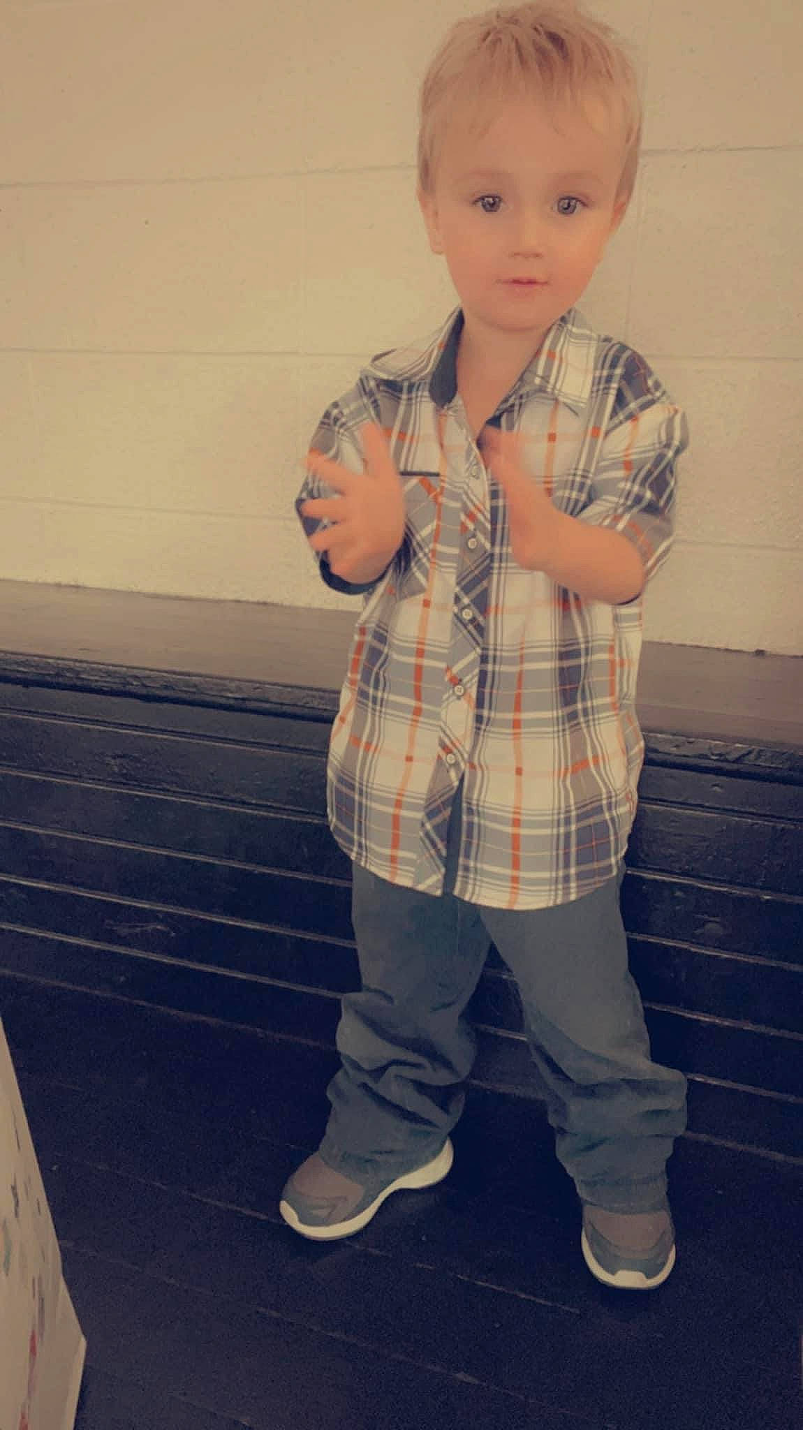 Carson is registered to the contest to win money with this photo: baby, blond, child, denim, dress_shirt, flooring, formal_wear, fun, gesture, happy, pattern, person, plaid, portrait_photography, sitting, sleeve, standing, tartan, toddler, toy