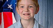Tanner is registered to the contest to win money with this photo: child, portrait, smiling, red_hair, blue_eyes, freckles, boy, american_flag, patriotic, shirt, button_up_shirt, wooden_wall, indoors, close_up, headshot, happy, standing, face, eyes, photography