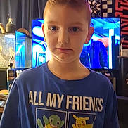 Tanner is registered to the contest to win money with this photo: child, boy, portrait, standing, indoors, pokemon, t_shirt, smiling, serious_expression, short_hair, face, person, television, plush_toys, neon_light, aquarium, blue_shirt, home, wood_paneling, photograph