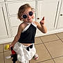 Milie participe au concours pour gagner de l'argent avec cette photo : child, toddler, sunglasses, black_top, white_skirt, plush_toy, indoor, tile_floor, cabinet, smiling, playful, fashion, cute, person, footwear, curly_hair, accessory, standing, happy, home