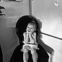 Milie a rejoint le concours — aidez-le/la à gagner de superbes lots ! child, girl, laughing, smiling, chair, black_and_white, vintage, indoor, happy, portrait, hands_on_face, barefoot, dress, tile_floor, shadow, plant, wall_art, home, seated, cute