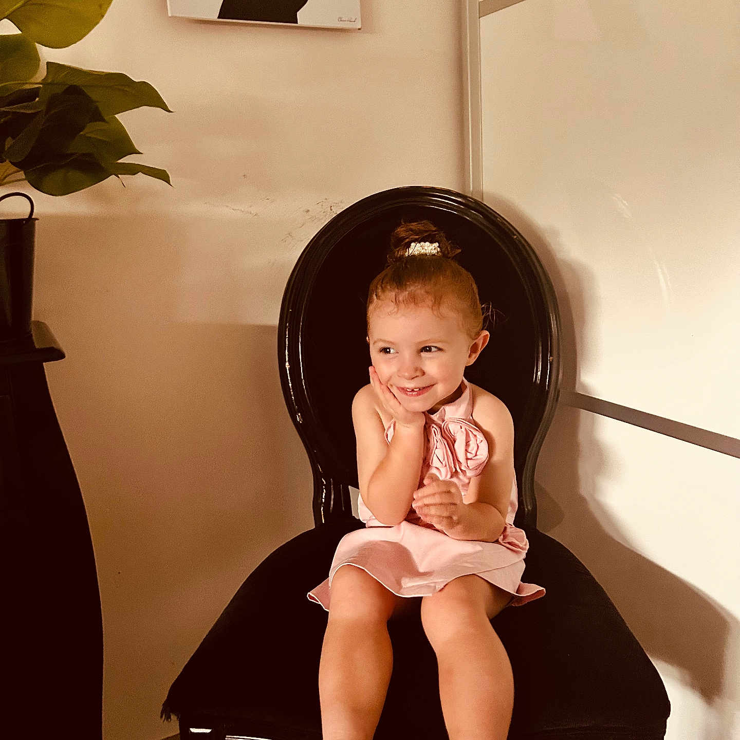Milie participe au concours pour gagner de l'argent avec cette photo : artwork, bare_legs, barefoot, black_chair, child, cute, decor, floor_tiles, furniture, girl, hair_bun, happy, indoor, light_shadow, pink_dress, plant, portrait, seated, smile, young_child