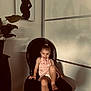 toddler, child, smile, pink_dress, black_chair, indoor, plant, painting, silhouette, shadow, wall, hair_tie, barefoot, furniture, room, portrait, happy, cute, sitting, home