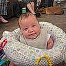 Lukas is registered to the contest to win money with this photo: baby, infant, child, smiling, portrait, sitting, activity_seat, toy, teether, yellow_toy, dog, pet, living_room, indoor, adult, phone, chair, carpet, bib, family