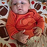 baby, infant, child, portrait, orange_outfit, pumpkin, autumn, blanket, lying_down, face, eyes, hands, serious_expression, indoors, cozy, textile, patterned_blanket, closeup, photography, safe
