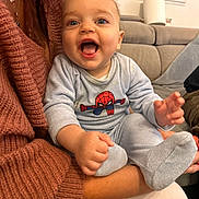 Kayden participe au concours pour gagner de l'argent avec cette photo : adult, arm, baby, child, clothing, couch, cute, fabric, footwear, happy, human_hand, indoor, infant, living_room, onesie, person, seat, smiling, sock, spiderman