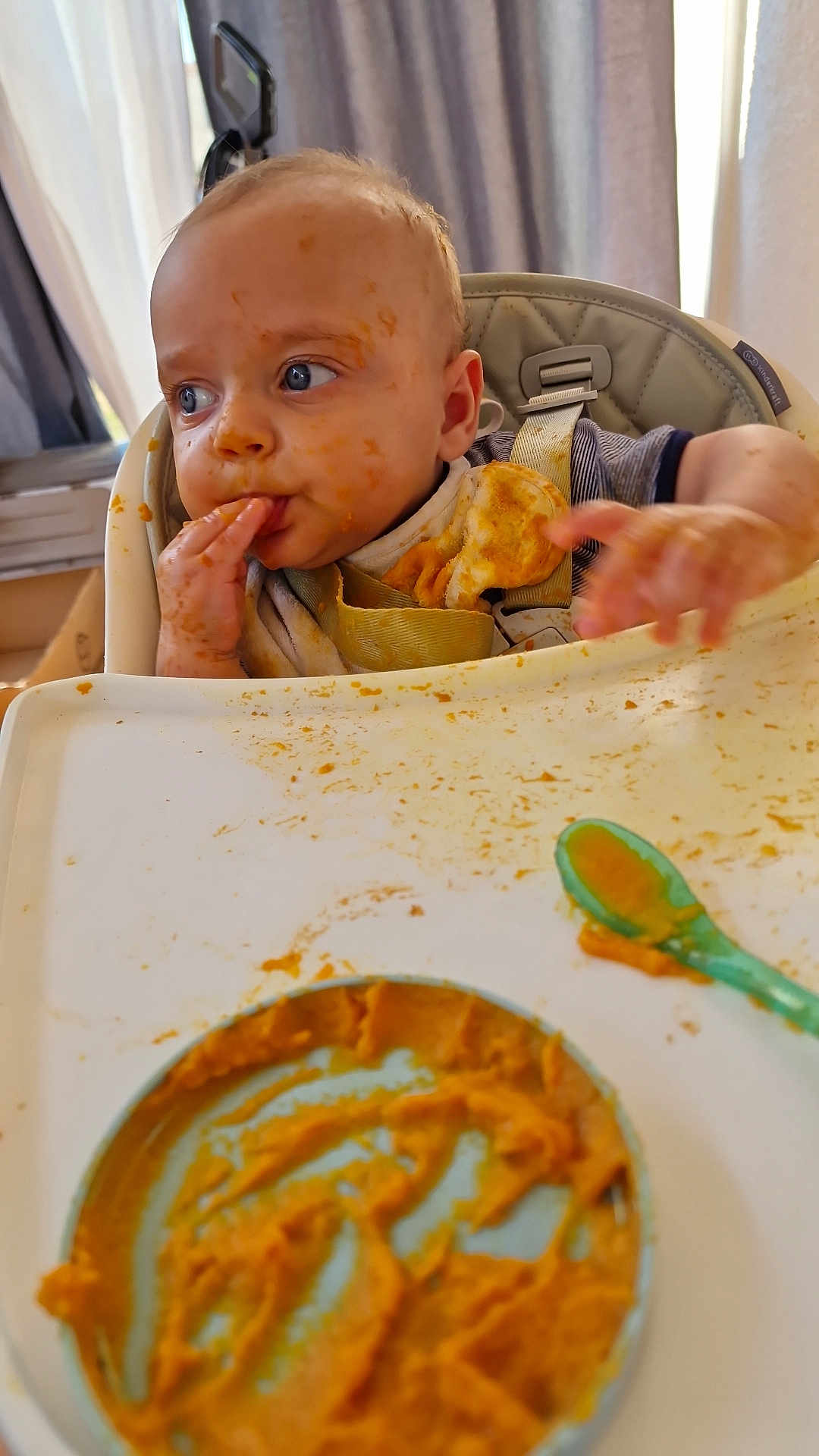 Kayden a rejoint le concours — aidez-le/la à gagner de superbes lots ! baby, high_chair, baby_food, messy, orange_food, face, hand, spoon, tray, feeding, child, blue_eyes, clothing, curtain, window, indoor, infant, cute, expression, person