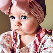 Laramie Kate joined the competition — help win amazing prizes! baby, infant, girl, headband, big_bow, blue_eyes, cheeks, portrait, closeup, pink, floral_dress, ruffles, looking_away, soft_light, indoor, pastel_background, skin, hand, cute, eyelashes