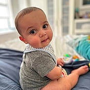Shir is registered to the contest to win money with this photo: baby, bed, blanket, cheeks, child, cute, eyes, face, furniture, home, indoor, infant, onesie, person, portrait, sitting, skin, smile, toy, young