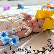 Elianna is registered to the contest to win money with this photo: baby, infant, yellow_bow, headband, lemon_pattern, dress, blue_flowers, blanket, toy, lying_down, cute, smiling, face, skin, child, soft_focus, indoor, decorations, colorful, happy