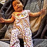 baby, infant, blanket, pajamas, clothing, patterned, lying_down, hand_motion, face, person, soft_texture, cute, indoors, child, sleepwear, footwear, pink, purple, yellow, relaxed
