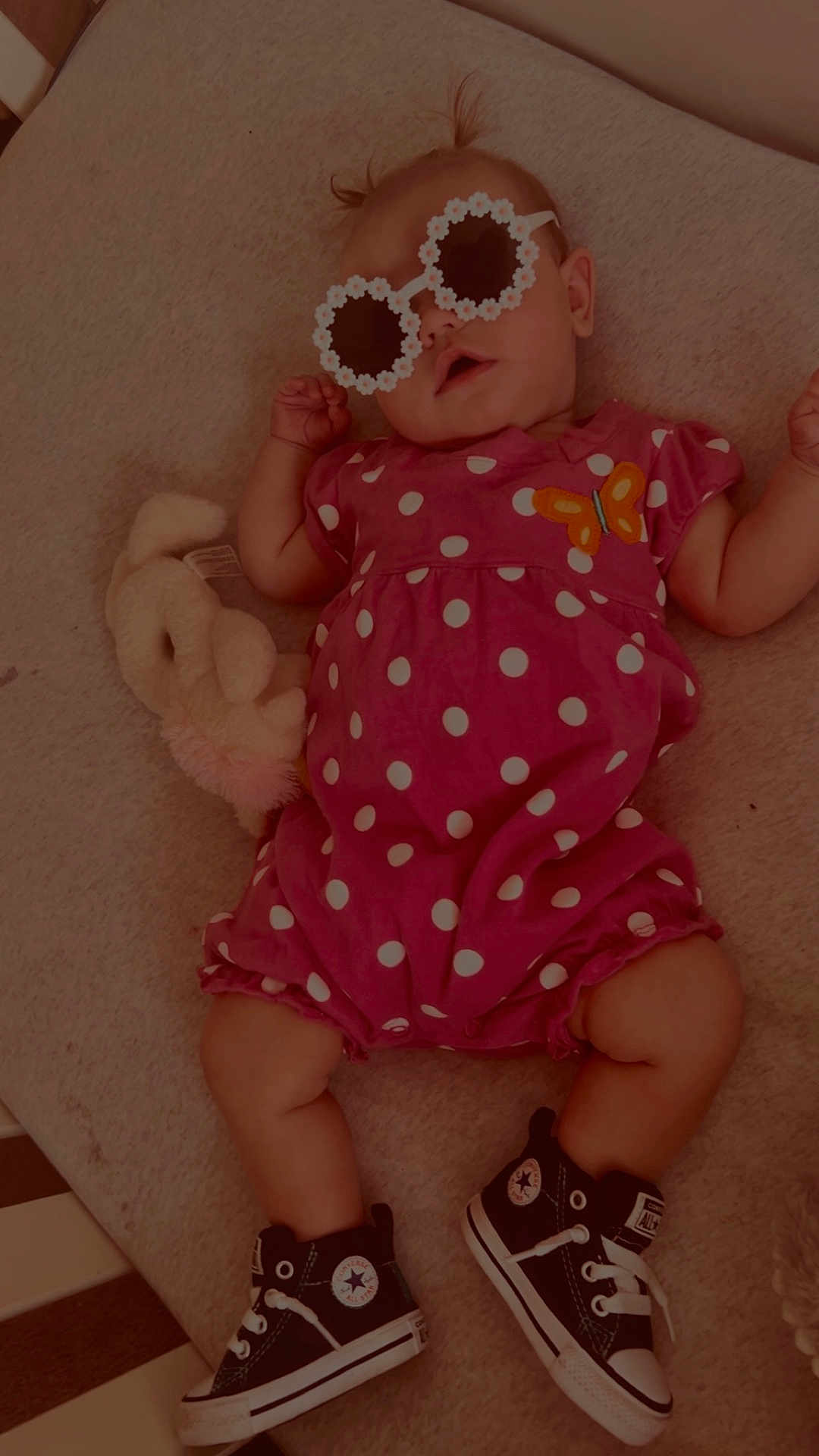 Rain is registered to the contest to win money with this photo: baby, infant, pink_outfit, polka_dot, butterfly_patch, sunglasses, flower_shaped, pigtails, black_sneakers, converse, plush_toy, cuddly_toy, soft_surface, cute, child, lying_down, indoors, fashion, footwear, accessories