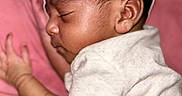 Junie is registered to the contest to win money with this photo: baby, infant, sleeping, portrait, side_profile, face, closed_eyes, curly_hair, brown_skin, white_shirt, pink_blanket, lying_down, indoors, close_up, peaceful, relaxed, child, photograph, soft_lighting, nap