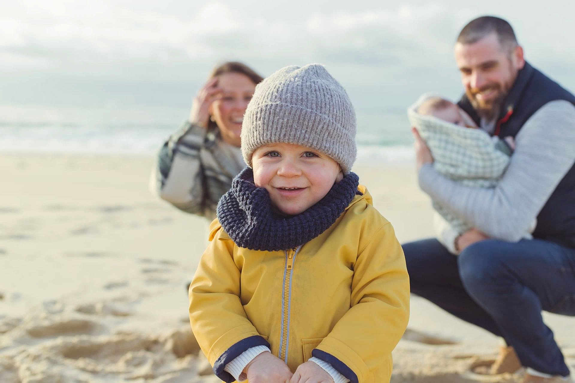 Milo participe au concours pour gagner de l'argent avec cette photo : toddler, child, family, beach, smiling, yellow_jacket, knit_hat, scarf, sand, ocean, mother, father, baby, blanket, outdoor, happy, portrait, people, casual_clothing, daytime