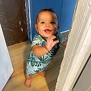 Jaden joined the competition — help win amazing prizes! baby, child, smiling, standing, indoor, doorway, wooden_floor, blue_wall, romper, clothing, person, hand, face, happy, cute, infant, toes, expression, young, reaching
