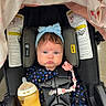 baby, car_seat, blue_eyes, headband, pacifier, bottle, blanket, onesie, heart_pattern, infant, child, sitting, baby_clothing, baby_accessory, feeding_bottle, car_seat_harness, pink, blue, cute, indoor