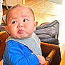 baby, child, pout, blue_shirt, bib, high_chair, wooden, indoor, face, expression, cute, infant, person, furniture, stroller, floor, tile, skin, head, hand