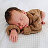 newborn, baby, sleeping, brown_sweater, knitted_clothing, cozy, soft_blanket, white_background, peaceful, infant, cute, portrait, hand, face, head, resting, child, indoors, relaxation, peace