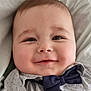 baby, infant, smiling, bow_tie, shirt, close_up, face, cheeks, eyes, eyelashes, pillow, bed, clothing, portrait, adorable, innocence, skin, mouth, nose, hair