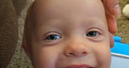 Everett joined the competition — help win amazing prizes! adult_hand, baby, blue_eyes, carpet, child, close_up, colorful_clothing, face, hand, happy, home, indoor, infant, laughing, photography, portrait, seated, shirt, smiling, teeth